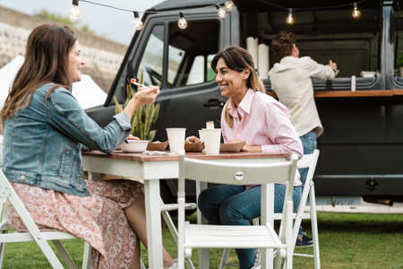 Happy mature women having fun eating in a street food truck outdoorの写真素材