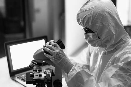 Female scientist working in research lab examining microorganisms through microscope - Science and...
