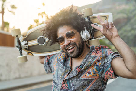 Happy Afro skater having fun listening to music with headphones during summer time - Youth people lifestyle conceptの写真素材