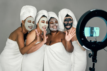 Happy multiracial females having skin care spa day while streaming on social network with mobile smartphone - People selfcare conceptの写真素材