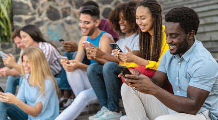 Young multiracial group of friends using mobile smartphone sitting on stairs - Youth millennial...