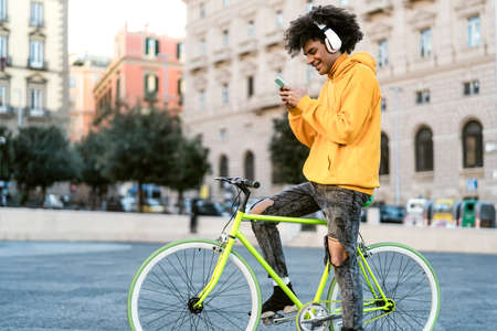 Happy African man using mobile smartphone outdoor - Young guy having fun riding with bike in the...
