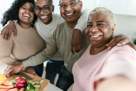 Happy Latin family having fun taking selfie while preparing healthy lunch in modern kitchen at home - Food and parents unity conceptの写真素材