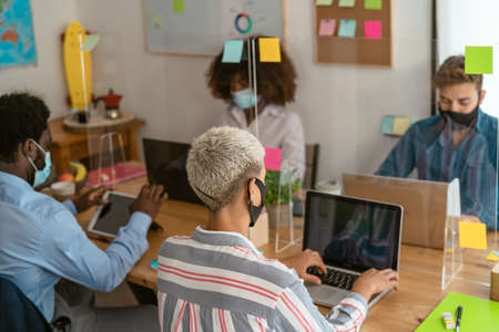 Young multiracial people using computer in co-working creative space while wearing face mask -...