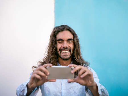 Happy long hair man having fun taking selfie with mobile smartphone outdoor
