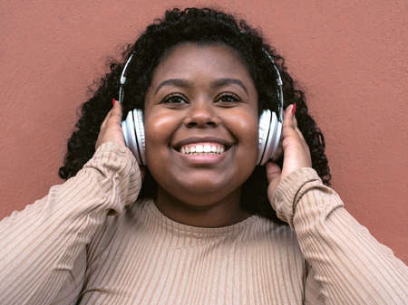 Happy Afro Latin girl having fun listening music with wireless headphones outdoorの写真素材