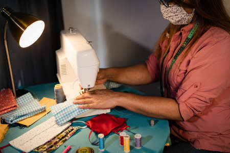 Hispanic woman working with sewing machine doing homemade face mask for preventing and stop corona virus spreading - Textile seamstress and homemade people work conceptの写真素材