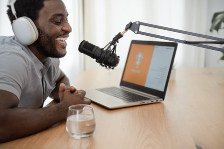 African man recording a podcast using microphone and laptop from his home studioの写真素材