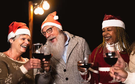 Happy senior friends celebrating Christmas holidays while toasting with red wine glasses on house patio partyの写真素材