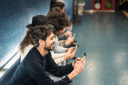 Young people using mobile smartphone while sitting in subway station waiting train - Youth millennial addicted to new technology conceptの写真素材