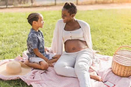 Happy playful Afro mother and son having fun in park doing a picnic together - Family love concept