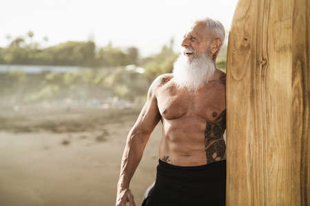 Senior male having fun surfing during sunset time - Fit retired man training with surfboard on the...