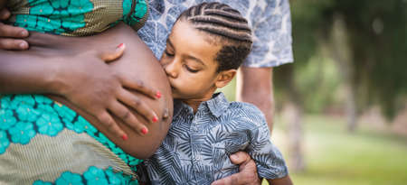 Happy African family expecting other baby - Close up child kissing belly of his pregnant mother - Parents love and maternity lifestyle conceptの写真素材