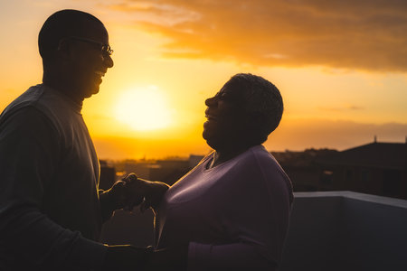 Happy Latin senior couple having romantic moment dancing on rooftop during sunset timeの写真素材
