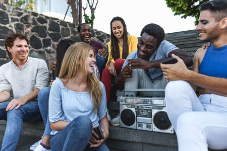 Young multiracial friends having fun listening music with vintage boombox stereo while sitting on city urban stairs - Youth millennial lifestyle conceptの写真素材