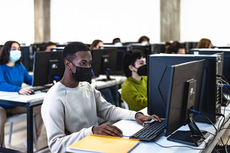 Young multiracial students taking an exam in high school while wearing face mask during corona virus pandemic - Education and technology conceptの写真素材