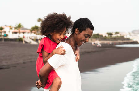 Happy Afro mother and daughter having fun on the beach during vacations - Lovely family lifestyle...