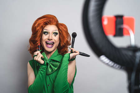 Happy drag queen social influencer vlogging online a makeup class with smartphone cam and ring ledの写真素材