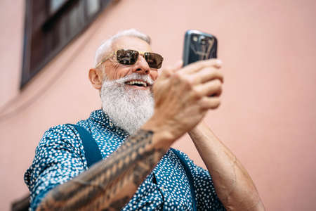 Happy trendy senior man having fun using mobile smartphone outdoor