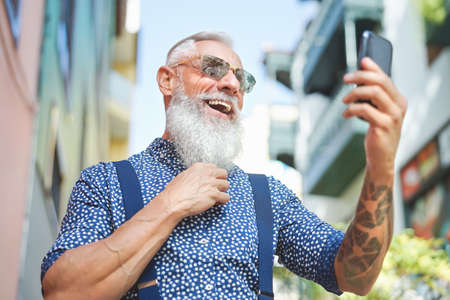 Happy trendy senior man having fun using mobile smartphone outdoor