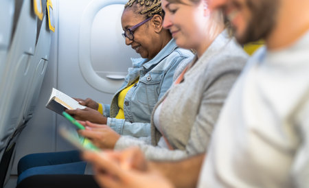 Passengers reading book and using mobile smartphones during airplane tripの写真素材