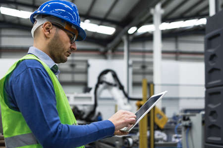 Engineer man working in robotic factory while monitoring the project on smart tablet - Tech industry...