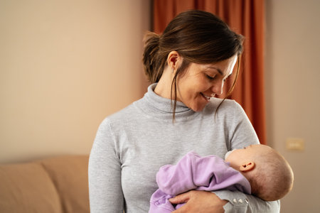 Happy mother taking care of her little baby sleeping in her arms at home - Concept family and motherhoodの写真素材