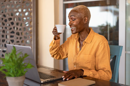 Happy African woman drinking a coffee while working with laptop at the cafe shopの写真素材