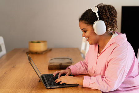 Young African girl using laptop listening podcast with headphones at home