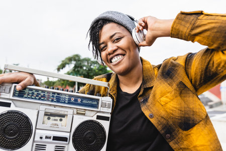 Happy African girl having fun listening to music with headphones and vintage stereo boomboxの写真素材