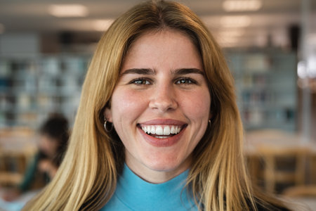 Happy young girl smiling into the camera while standing inside university libraryの写真素材