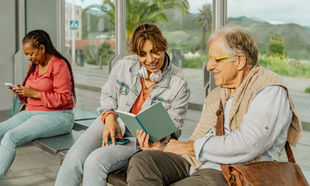 Multiracial people reading a book while waiting at tram station in the cityの写真素材