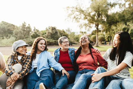 Happy multi generational group of women with different ethnicities having fun sitting on grass in a public park - Females empowerment conceptの写真素材