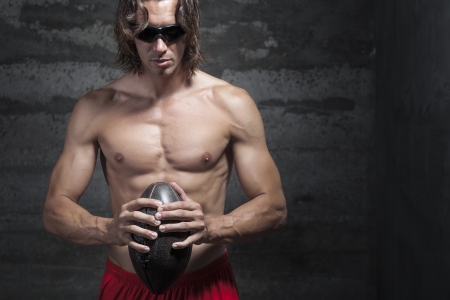 bare chested long hair muscle man is wearing sunglasses and holding football ball in handsの写真素材