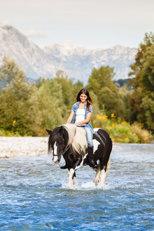 Beautiful Female sitting on horse while crossing river in a mountainous landscapeの写真素材