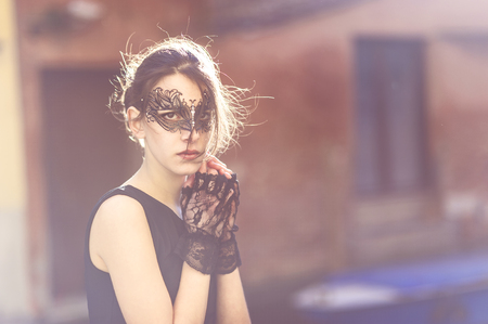 Half Body Shot of an Elegant Woman wearing Black Masquerade Mask and Lace Gloves with Hands on the Face While Looking at the Camera.の写真素材