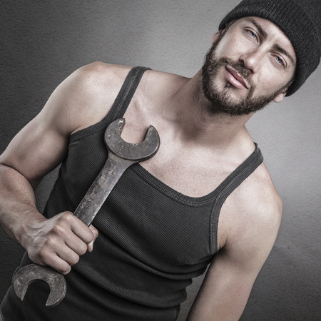 Handsome rough casual man standing and holding a wrench over a textured grey backgroundの写真素材