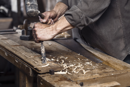 Carpenter with a hammer and chisel on the wooden workbench in carpentry