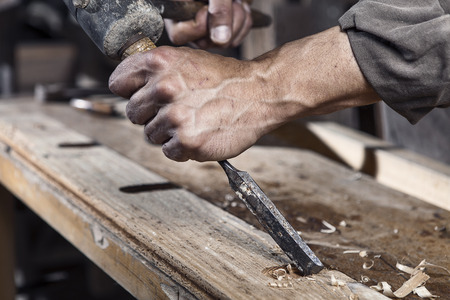 Hands of carpenter with chisel in the hands on the workbench in carpentry