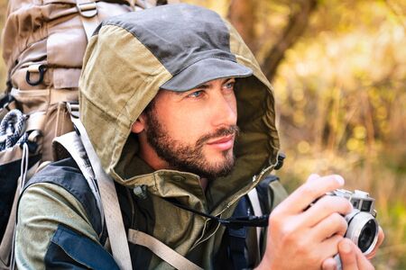 Handsome young man portrait, with vintage camera. Hooded guy hiking in the forest. Active lifestyle, tourism in nature.の写真素材