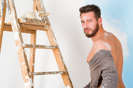 Portrait of handsome seductive paint-splattered painter with vintage ladder, undressing and looking at cameraの写真素材