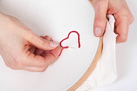Close up of Woman Hands sewing a Red Heart Shaped Decoration on White Fabric