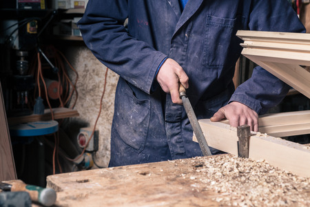 Close-up of a Carpenter working on a Wooden Window Frame with a File in his Workshop; Selective...