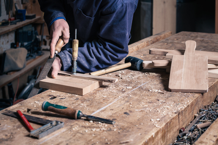 Close-up of a Carpenter working on a Wooden Cutting Board with a File in his Workshop; Selective...