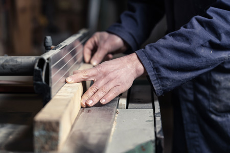Close up of Carpenter's hands cutting wood with tablesaw in workshop; selective focus