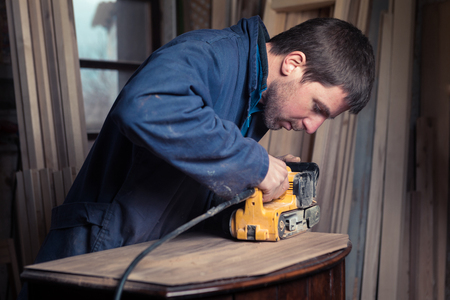 Portrait of Carpenter restoring old wooden furniture with belt sander in his Wood Shopの写真素材