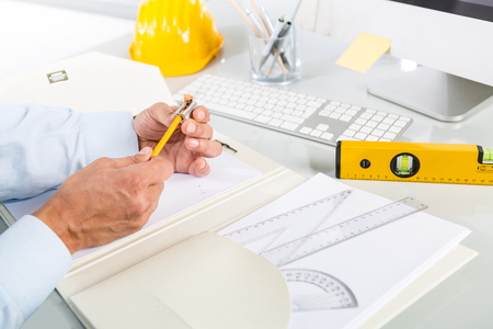 Close-up Of Architect Hands Sharpening a Yellow Pencil; Yellow Safety Helmet, Level and toolsの写真素材