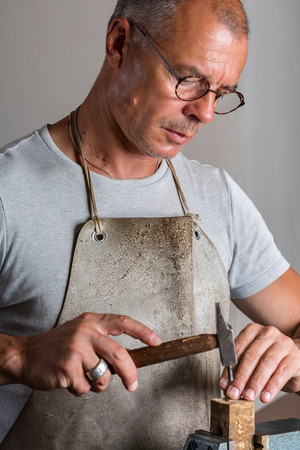 Portrait of Adult Male Goldsmith Shaping Thin Silver Pieces with Hammer at his Workshopの写真素材