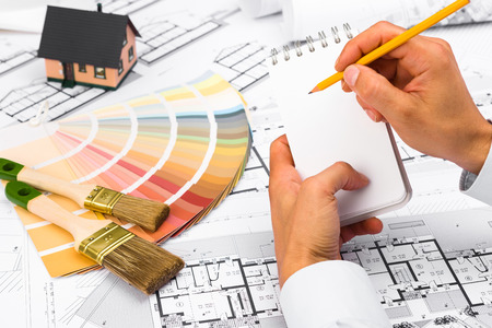 Male Hands writing on notebook; Construction plans with Color Palette and Miniature House on...