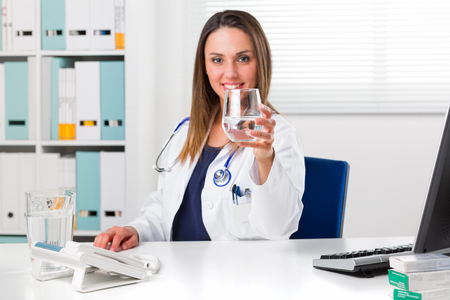 Portrait of Smiling Female Doctor offering a glass of water in her Office; Detox and Cleansing conceptの写真素材
